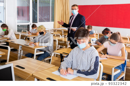Teacher man in protective mask helping students during lesson 93322342