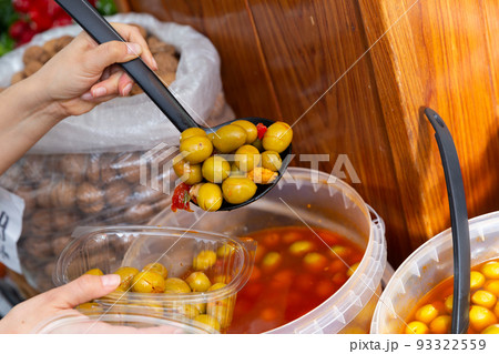 Female hands putting marinated olives from plastic bucket into container in store Female hands putting marinated olives from plastic bucket into container in store 93322559