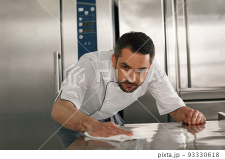 Young handsome male chef cleaning his workplace on kitchen in restaurant 93330618