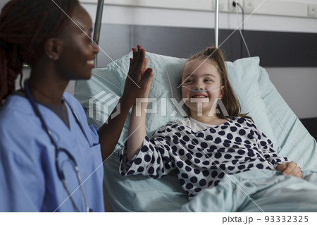 African american nurse doing high five gesture with sick girl resting in hospital pediatric ward patient bed. Childcare healthcare facility staff high fiving ill kid under medical treatment. African american nurse doing high five gesture with sick girl resting in hospital pediatric ward patient bed. Childcare healthcare facility staff high fiving ill kid under medical treatment. 93332325