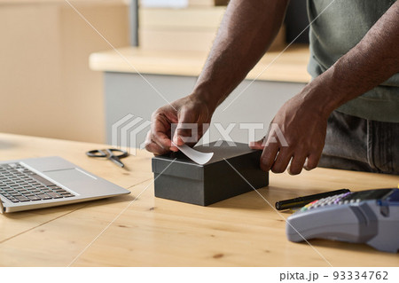 Close-up of worker packing order in the box at table and sticking note with track number on it 93334762