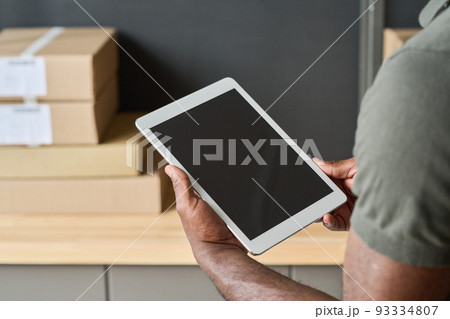 Close-up of warehouse worker checking track numbers of parcels on digital tablet during his work in warehouse 93334807