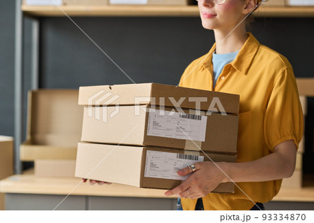 Close-up of worker carrying parcels in cardboard boxes for future delivery Close-up of worker carrying parcels in cardboard boxes for future delivery 93334870