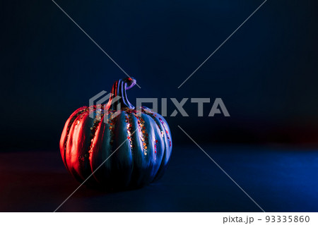 Decorative pumpkin with orange sparkles in neon red and blue light on the dark. Halloween decor and background with copy space. Selective focus 93335860