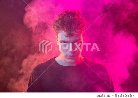 Smoke enveloped young man. Model looking at camera isolated over magenta background with clouds of smoke. Concept of mental health, art, emotions 93335867