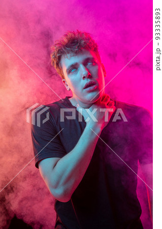 Suffocate in the smoke. Scared young man with stressed emotions isolated over pink background with clouds of smoke. Concept of facial expression, emotions Suffocate in the smoke. Scared young man with stressed emotions isolated over pink background with clouds of smoke. Concept of facial expression, emotions 93335893