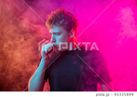 Suffocate in the smoke. Scared young man with stressed emotions isolated over pink background with clouds of smoke. Concept of facial expression, emotions Suffocate in the smoke. Scared young man with stressed emotions isolated over pink background with clouds of smoke. Concept of facial expression, emotions 93335899