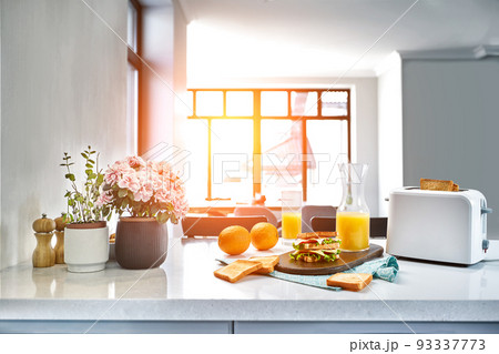 White electric bread toaster with orange juice with sandwich on kitchen table. Breakfast in the cozy kitchen. Sun flare 93337773