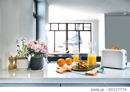 White electric bread toaster with orange juice with sandwich on kitchen table. Breakfast in the cozy kitchen. White electric bread toaster with orange juice with sandwich on kitchen table. Breakfast in the cozy kitchen. 93337774