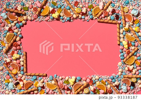 Multicolored glazed dragees and other sweets are arranged in the form of a frame on a coral background. 93338187