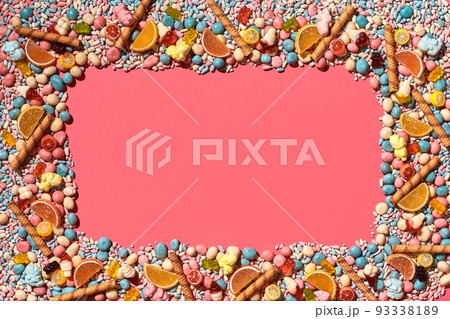Multicolored glazed dragees and other sweets are arranged in the form of a frame on a coral background. Multicolored glazed dragees and other sweets are arranged in the form of a frame on a coral background. 93338189