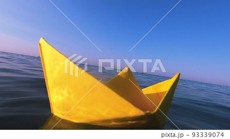 Yellow paper boat floats on surface of blue water waves of sea close-up. Clear blue sky on sunny summer day. Concept adventures travelling vacation holiday rest tourism voyager dream. Slow motion 93339074