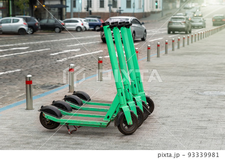 Many modern green electric scooters sharing parked city street. Self-service street transport rental service. Rent urban mobility vehicle with smartphone application. Zero emission green eco energy Many modern green electric scooters sharing parked city street. Self-service street transport rental service. Rent urban mobility vehicle with smartphone application. Zero emission green eco energy 93339981