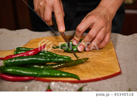 Details: Hands of chef or housewife using kitchen knife cutting red and green chili pepper on a chopping board. Slicing food, preparing spicy ingredients for canning or pickling. Raw vegan vegetables Details: Hands of chef or housewife using kitchen knife cutting red and green chili pepper on a chopping board. Slicing food, preparing spicy ingredients for canning or pickling. Raw vegan vegetables 93340518
