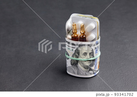 Tablets and ampoules in a blister pack are wrapped in one hundred dollar bills of money, fastened with an elastic band Tablets and ampoules in a blister pack are wrapped in one hundred dollar bills of money, fastened with an elastic band 93341702