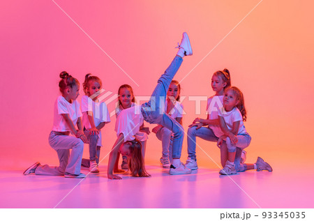 Group of children, school age girls in sportive casual style clothes dancing in choreography class isolated on pink background in yellow neon light. Group of children, school age girls in sportive casual style clothes dancing in choreography class isolated on pink background in yellow neon light. 93345035