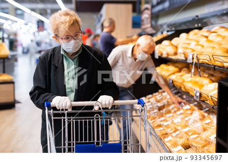 older woman with glasses chooses buns and bread in supermarket bakery older woman with glasses chooses buns and bread in supermarket bakery 93345697