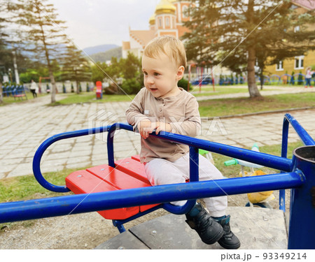 A cute boy of one and a half years rides on a swing in the playground. Children's entertainment. Selective focus 93349214
