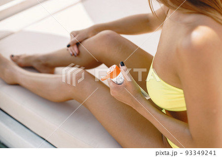 Woman applying sunscreen lotion on her legs, while lying on the sunbed. 93349241