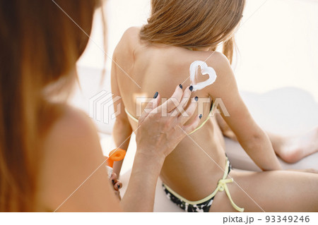 Mother and daughter going to sunbathe. Parent applying sunscreen on chils, sitting by poolside. 93349246
