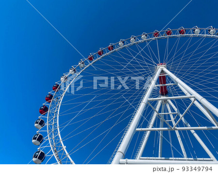 amusement park. ferris wheel made of white metal. a huge wheel with booths for tourists in white and red. ferris wheel against blue clear sky amusement park. ferris wheel made of white metal. a huge wheel with booths for tourists in white and red. ferris wheel against blue clear sky 93349794
