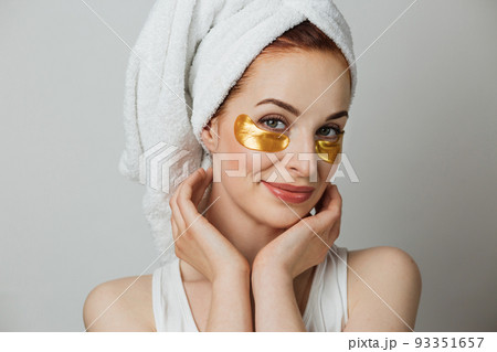 Portrait of young woman in towel touching with her hands golden hydrogel patches under eyes. Portrait of young woman in towel touching with her hands golden hydrogel patches under eyes. 93351657
