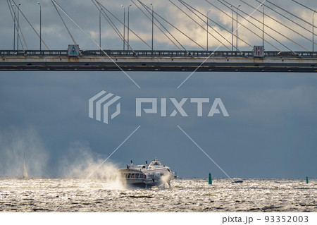 a high-speed passenger hydrofoil boat passes under a cable-stayed bridge in sunny weather, dark storm clouds in the background a high-speed passenger hydrofoil boat passes under a cable-stayed bridge in sunny weather, dark storm clouds in the background 93352003