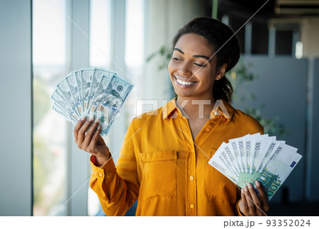 Portrait of excited businesswoman holding bunches of dollar cash and smiling, posing in office interior 93352024