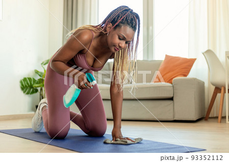 African american woman in sportswear cleaning yoga mat after workout at home, using detergent spray African american woman in sportswear cleaning yoga mat after workout at home, using detergent spray 93352112