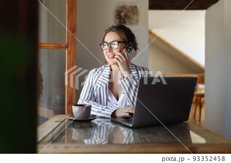 Happy young businesswoman sitting at table with laptop, holding mobile phone call with client in office. Skilled manager saleswoman calling customer, giving professional consultation. Happy young businesswoman sitting at table with laptop, holding mobile phone call with client in office. Skilled manager saleswoman calling customer, giving professional consultation. 93352458