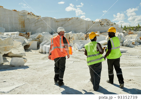 Back view of three workers of marble quarry moving down territory of factory 93352739