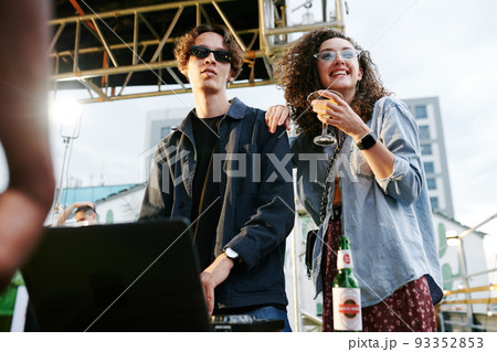 Happy young woman with cocktail standing next to her boyfriend making music 93352853