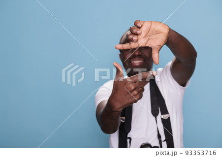 Confident professional photographer doing frame gesture with hands while having modern camera on blue background. Young guy with DSLR device gesturing taking photo with hands. Studio shot Confident professional photographer doing frame gesture with hands while having modern camera on blue background. Young guy with DSLR device gesturing taking photo with hands. Studio shot 93353716