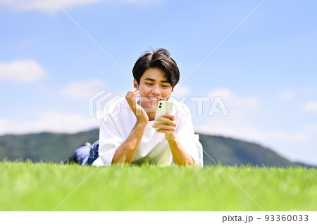 芝生にうつ伏せでスマホを操作する男性 93360033