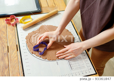 View of woman hands cooking homemade cookies from rolled gingerbread dough with culinary molds View of woman hands cooking homemade cookies from rolled gingerbread dough with culinary molds 93361847