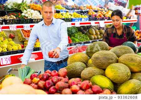 Focused man choosing pomegranates on counter in greengrocery store Focused man choosing pomegranates on counter in greengrocery store 93362608