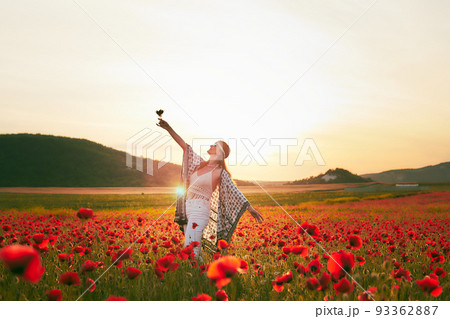 A woman eating strawberries at sunset in a field of poppies. Front view. 93362887