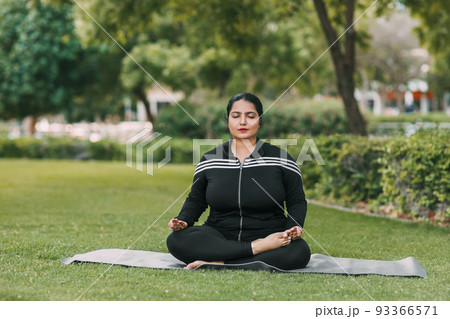 A young Indian woman meditates with her eyes closed in the open air. A young Indian woman meditates with her eyes closed in the open air. 93366571