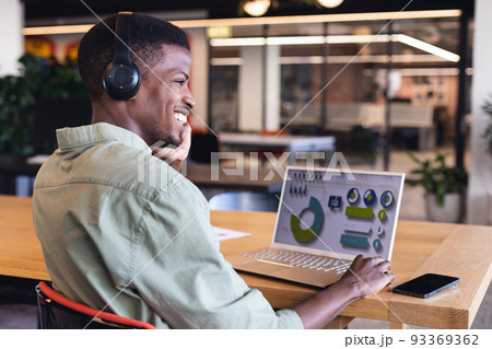 Smiling african american young businessman talking on phone while planning strategy on laptop 93369362