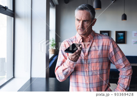 Serious caucasian mature businessman talking on smart phone speaker by window at creative office 93369428