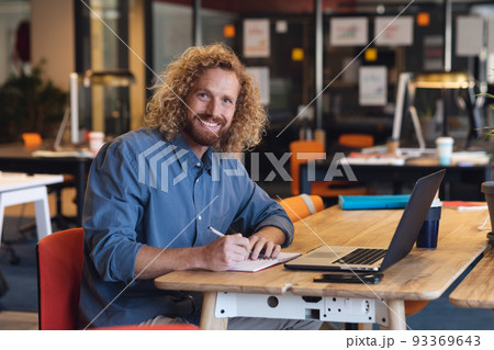 Portrait of young caucasian businessman writing in diary at desk in creative office 93369643