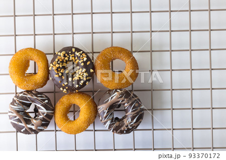 Overhead view of various fresh donuts on cooling rack over white background 93370172