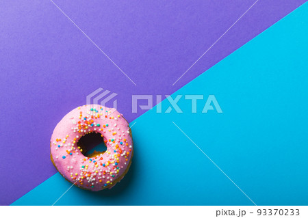 Directly above view of fresh pink donut with sprinklers by copy space against two tone background 93370233