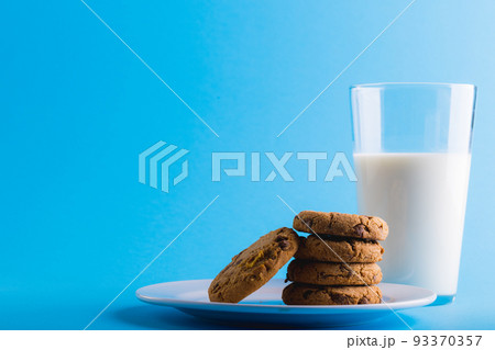 Close-up of milk glass with cookies against blue background, copy space Close-up of milk glass with cookies against blue background, copy space 93370357