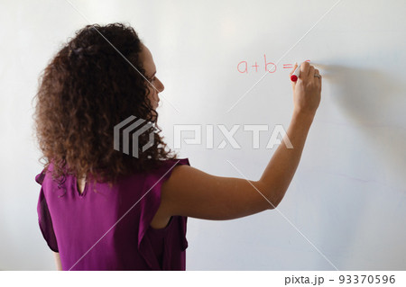 Caucasian young female teacher writing formula on whiteboard during math class in school 93370596