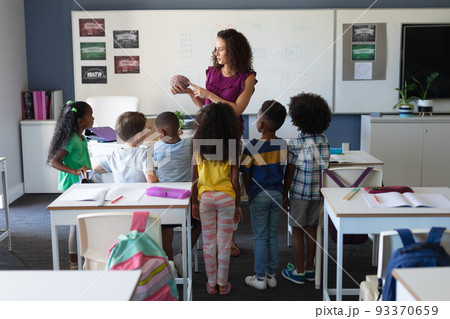 Multiracial elementary school students looking at caucasian young female teacher showing brain model 93370659
