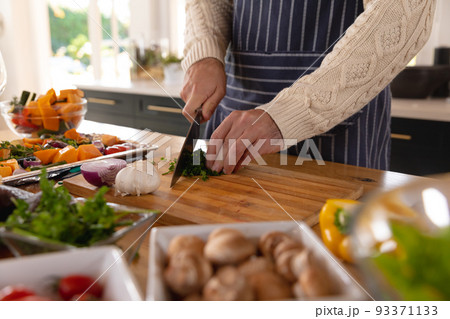 Midsection of caucasian man preparing food, chopping vegetables wearing apron in kitchen Midsection of caucasian man preparing food, chopping vegetables wearing apron in kitchen 93371133