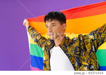 Happy biracial man holding lgbt rainbow flag and smiling on purple background 93371414
