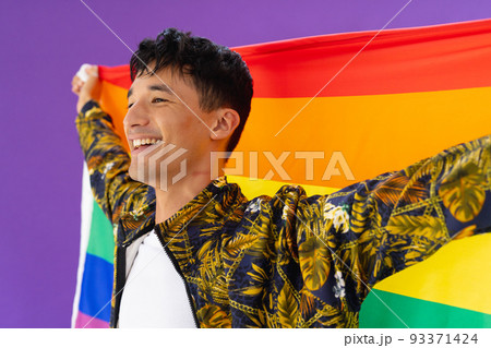 Happy biracial man holding lgbt rainbow flag and smiling on purple background 93371424