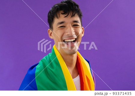 Portrait of happy biracial man holding lgbt rainbow flag and smiling on purple background Portrait of happy biracial man holding lgbt rainbow flag and smiling on purple background 93371435